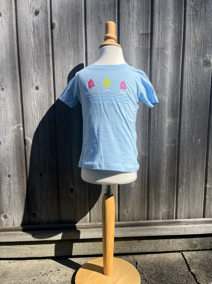 Light blue t-shirt with colorful designs on a mannequin against a wooden fence.