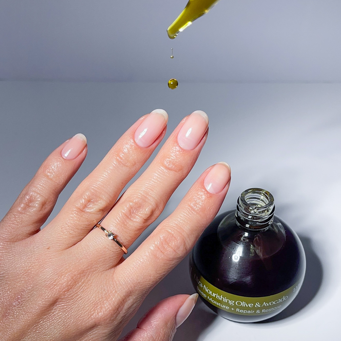 Applying Olive & Avocado cuticle oil with the dropper to a nude manicure