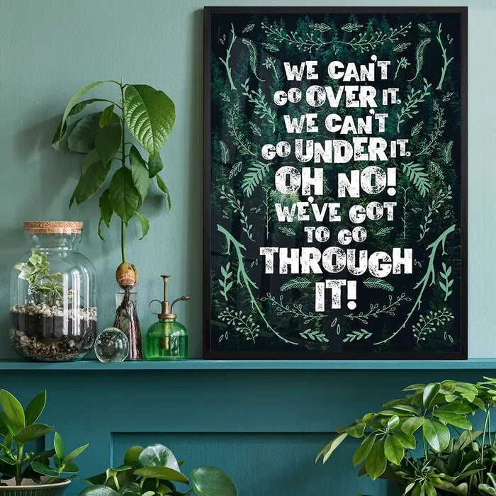 Green typography print with "We Can't Go Over It" quote, framed in black, on a teal wall.