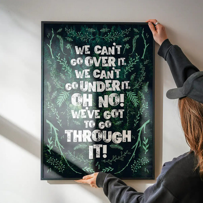 Green typography print with "We Can't Go Over It" quote, framed in black, held against a white wall.