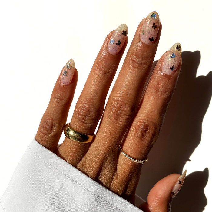 Wings of Dawn bronze butterfly glitter over a sheer nude manicure with gold rings