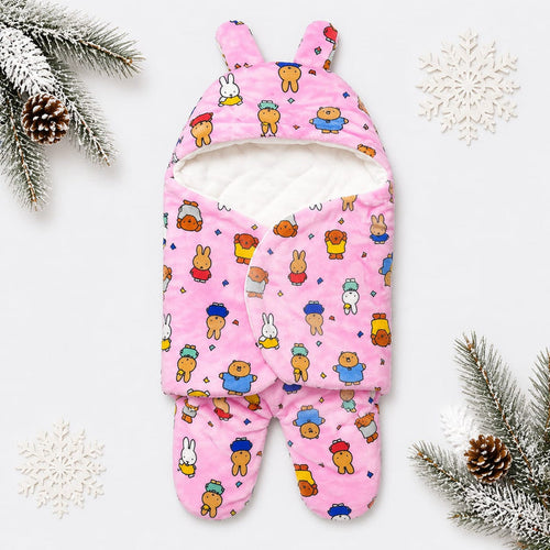 A pink footed baby sleep sack with bunny ears, featuring a playful cartoon bear and bunny pattern, styled on a white background with winter-themed pine branches and snowflakes.