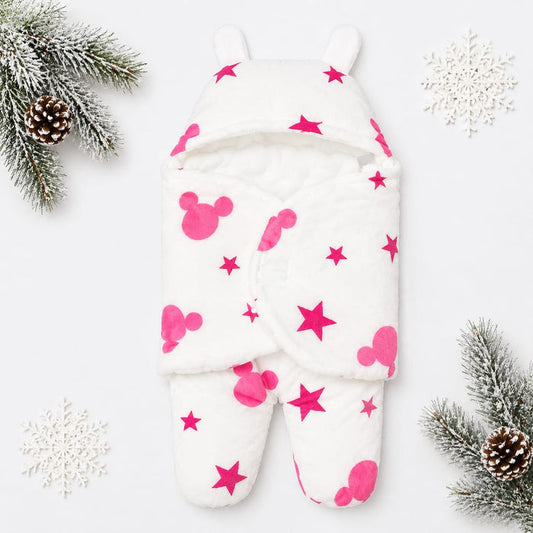 A white footed baby sleeper with pink Mickey Mouse-style shapes and stars, photographed flat on a white background with decorative pine branches and snowflakes around it.