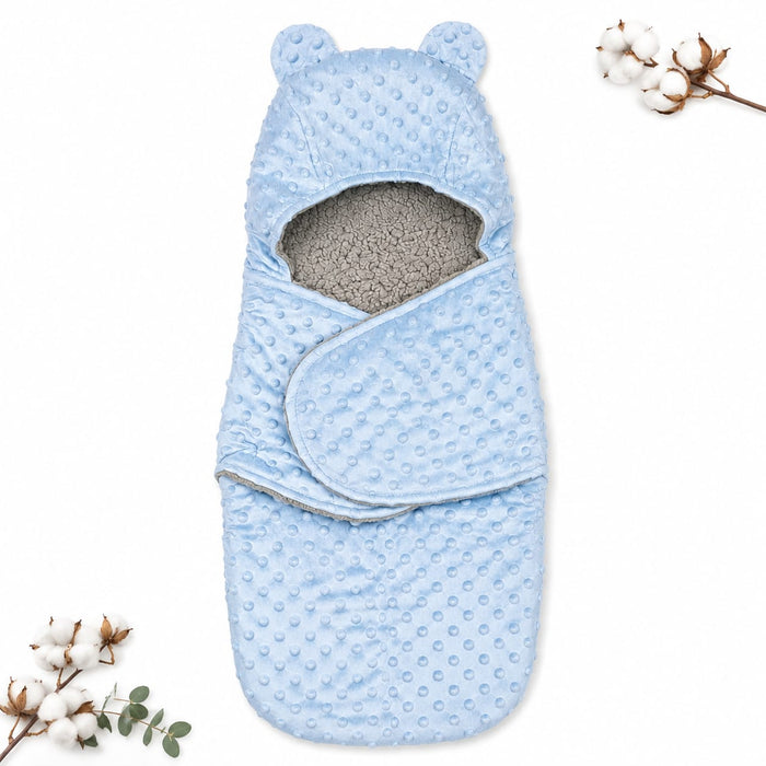 A light blue baby swaddle wrap with a textured minky dot pattern, featuring bear ears on the hood and a soft gray fleece lining. The swaddle is displayed flat on a white background with decorative cotton bolls in the corners.