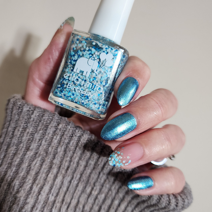 Winter Wishes confetti glitter over a metallic blue manicure, holding the bottle